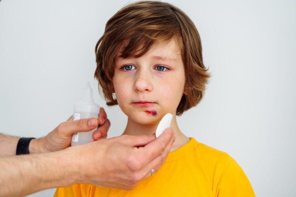 Dad doctor father treats bruised wound on his son school boy kid face. Man cleans addresses the sore