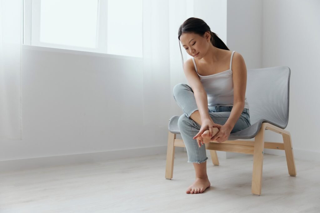 Full body shot suffering tanned beautiful young Asian woman touch pain foot massaging feet at home